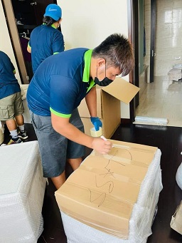 Two movers lifting a large sofa wrapped in protective plastic.